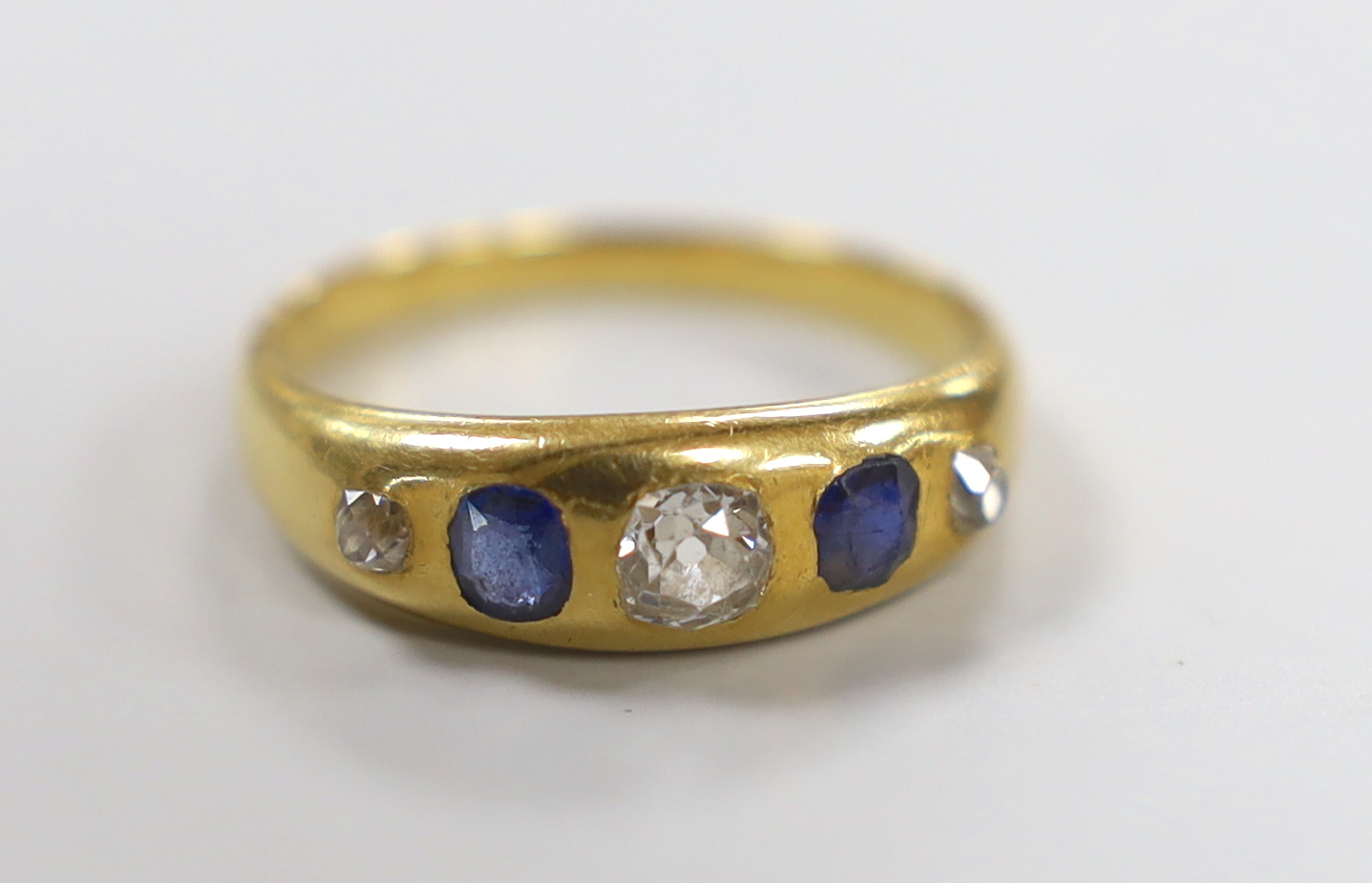 A yellow metal and gypsy set three stone diamond and two stone sapphire set half hoop ring, size S/T, gross weight 5.6 grams.